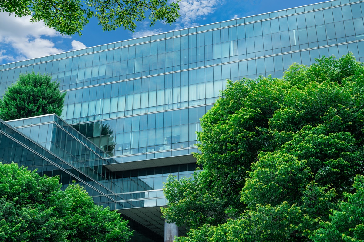 Modern glass building surrounded by lush green trees under a blue sky, symbolizing sustainable or ESG investment.