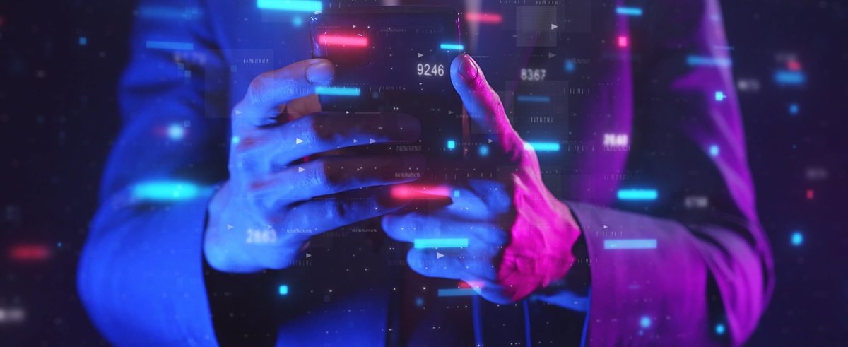 Hands holding a mobile phone with digital overlays of data and numbers in blue and pink on a dark background.